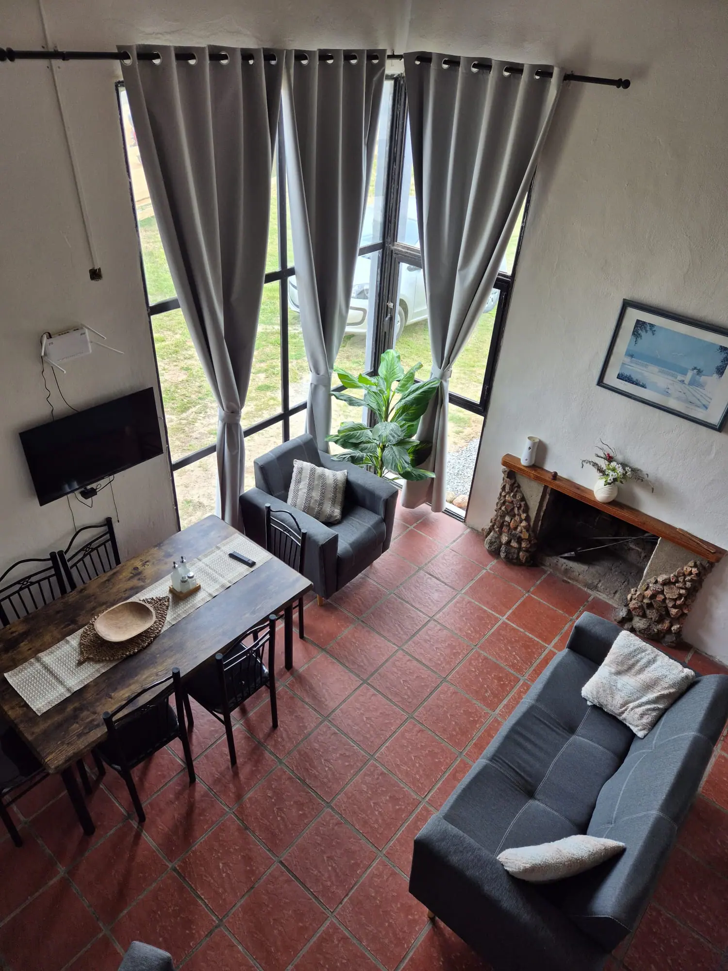 Living y comedor vistos desde arriba: mesa de madera para seis, sillón, estufa a leña y ventanal