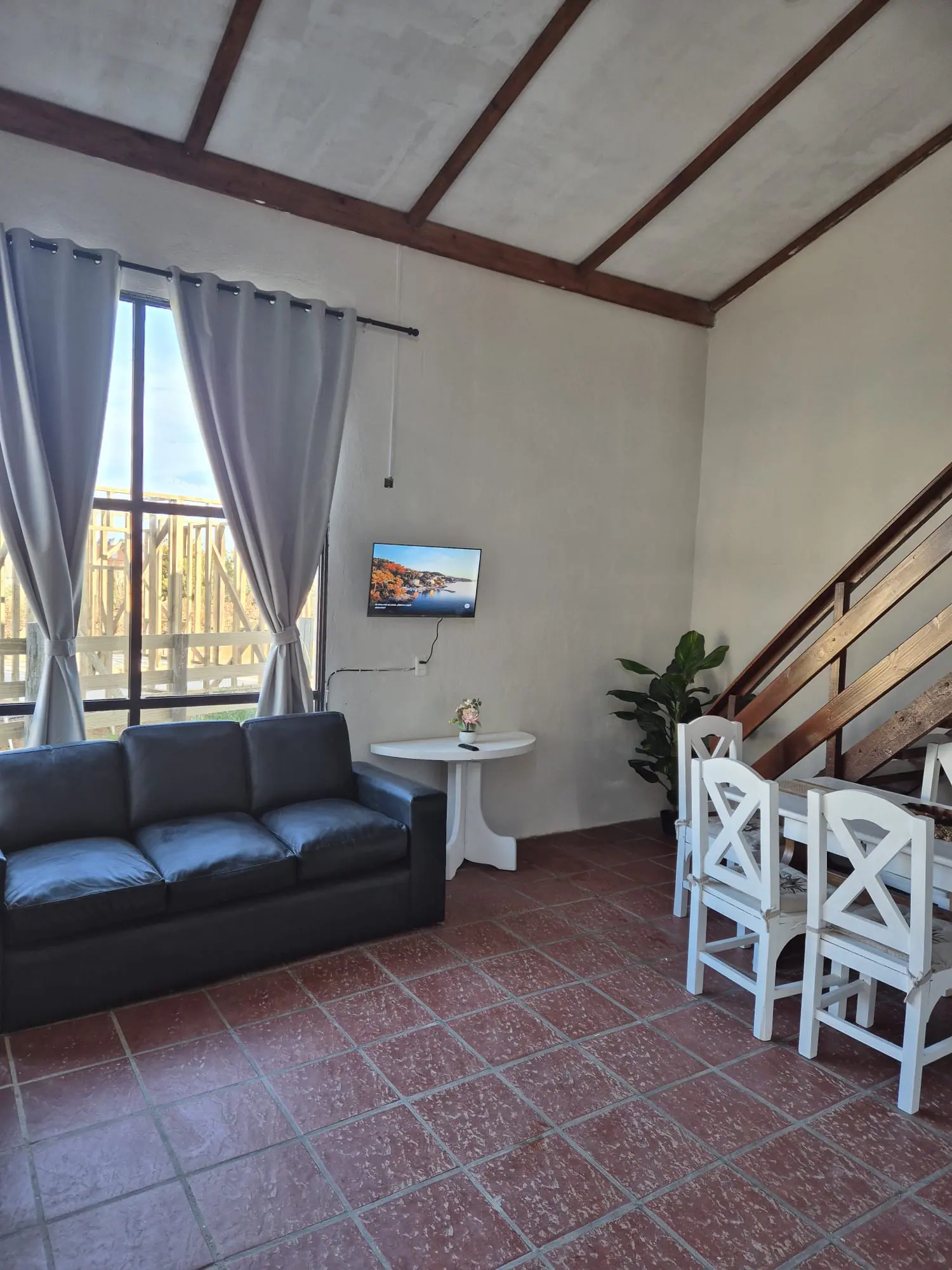 Living con sillón, televisor, comedor con sillas blancas y escalera de madera al entrepiso