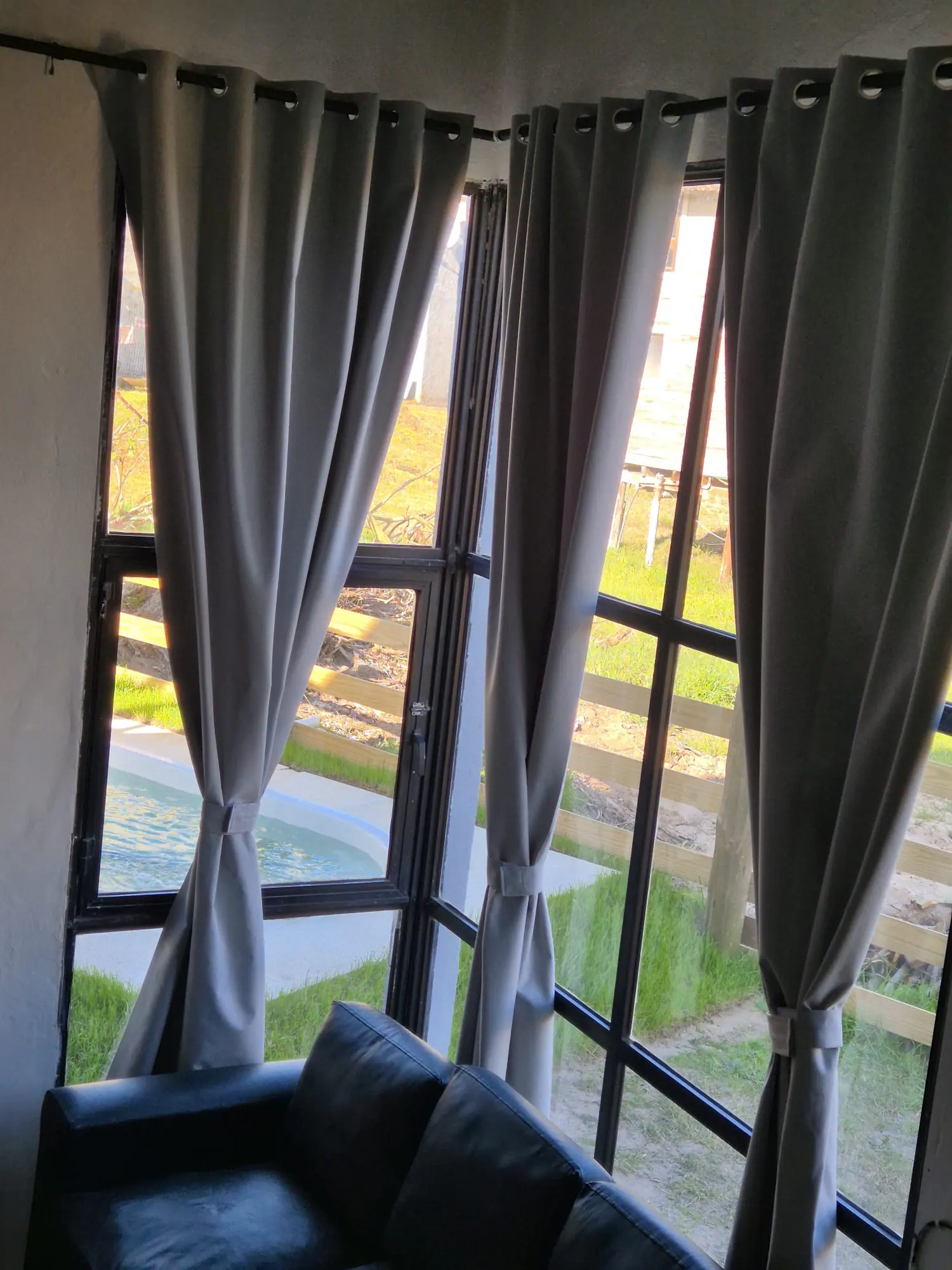 Ventanal con cortinas y vista al jardín y a la piscina desde el living